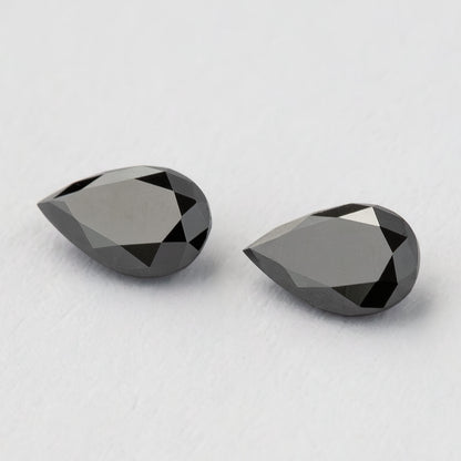Angled view of the black pear-shaped diamond pair, with broad pale reflections across their tables.