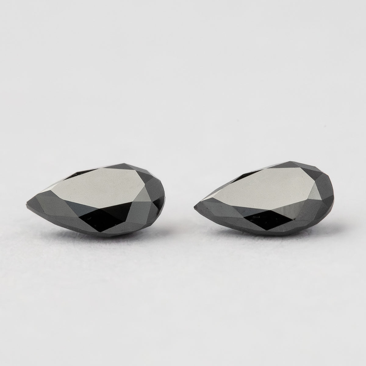 Low side view of the black pear-shaped diamonds, showing the profiles and faceted edges of both stones.