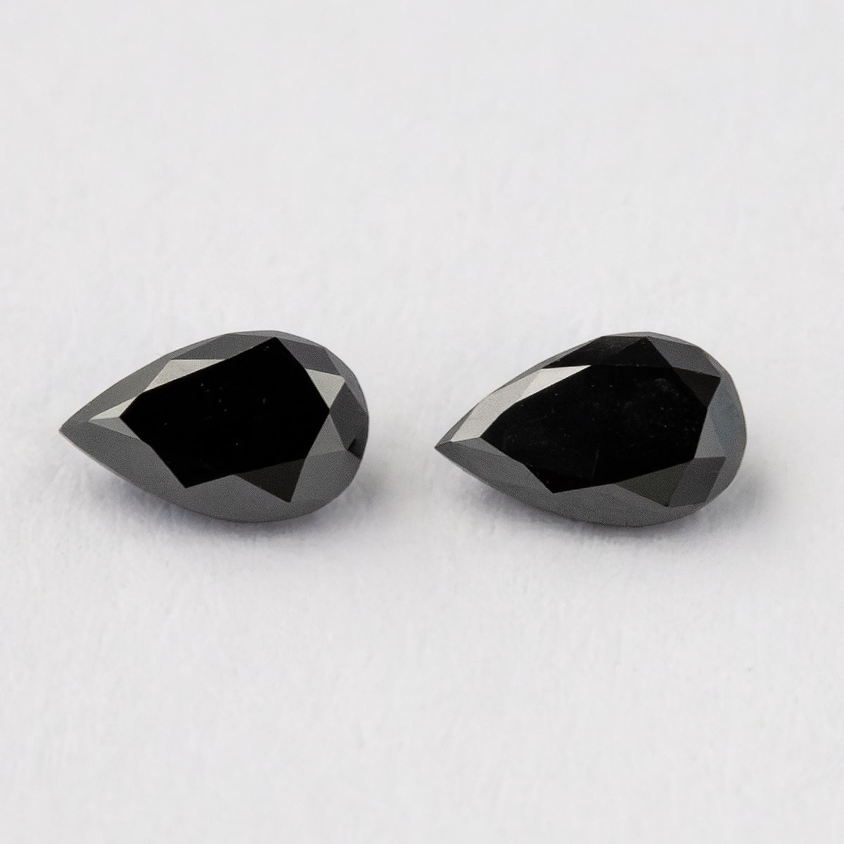 Black pear-shaped diamond pair viewed from above at a slight angle, with both pointed outlines visible.