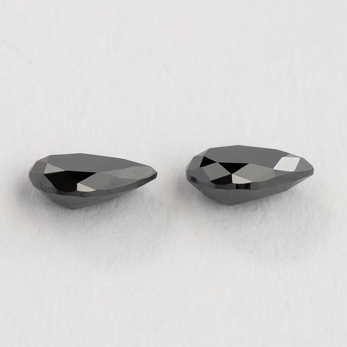 The black pear-shaped diamond pair from a shallow profile angle, with their edges and depth visible.