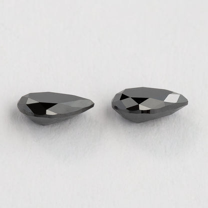 The black pear-shaped diamond pair from a shallow profile angle, with their edges and depth visible.