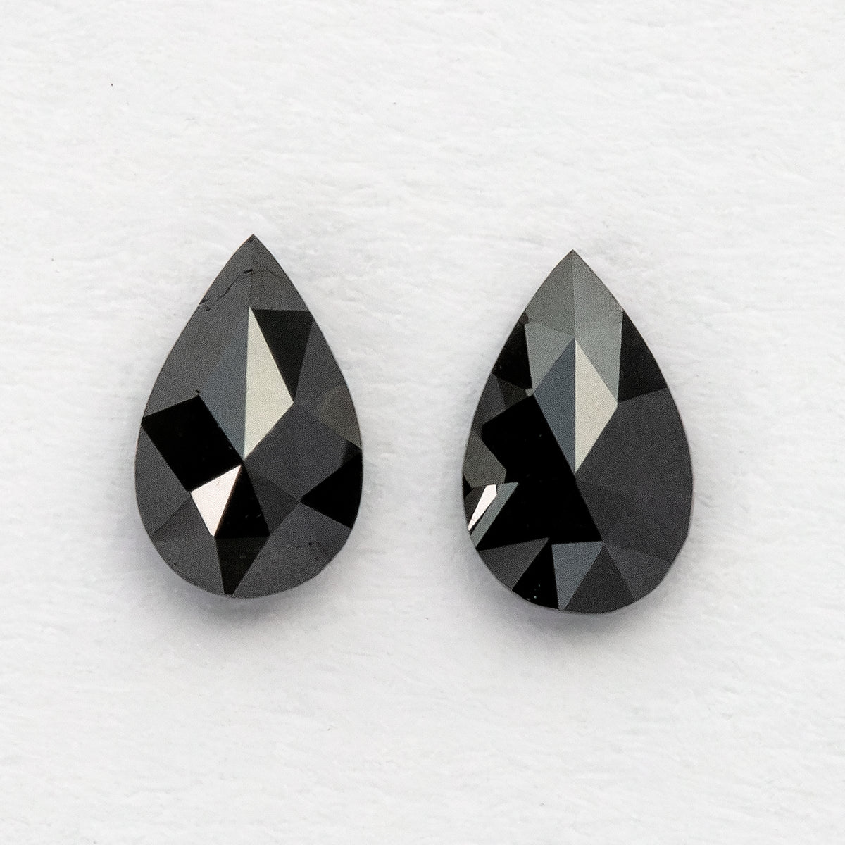 Reverse view of two black pear-shaped diamonds, showing the pointed, triangular pavilion facets rather than their flat tables.