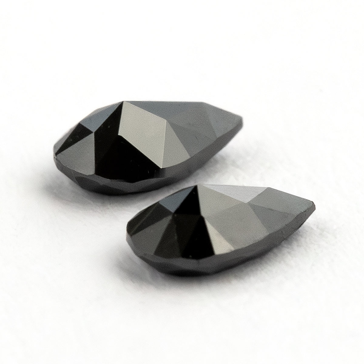 The black pear-shaped diamond pair tilted from the reverse side, with bright reflections across the pavilion facets.