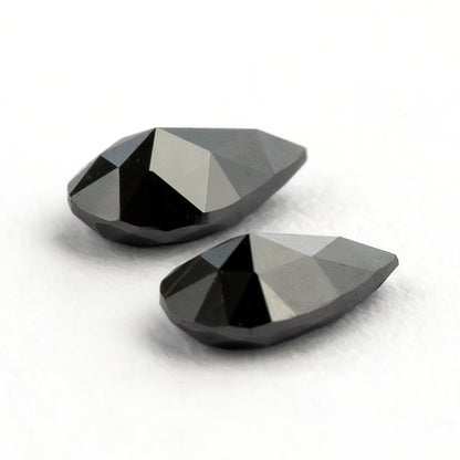 The black pear-shaped diamond pair tilted from the reverse side, with bright reflections across the pavilion facets.