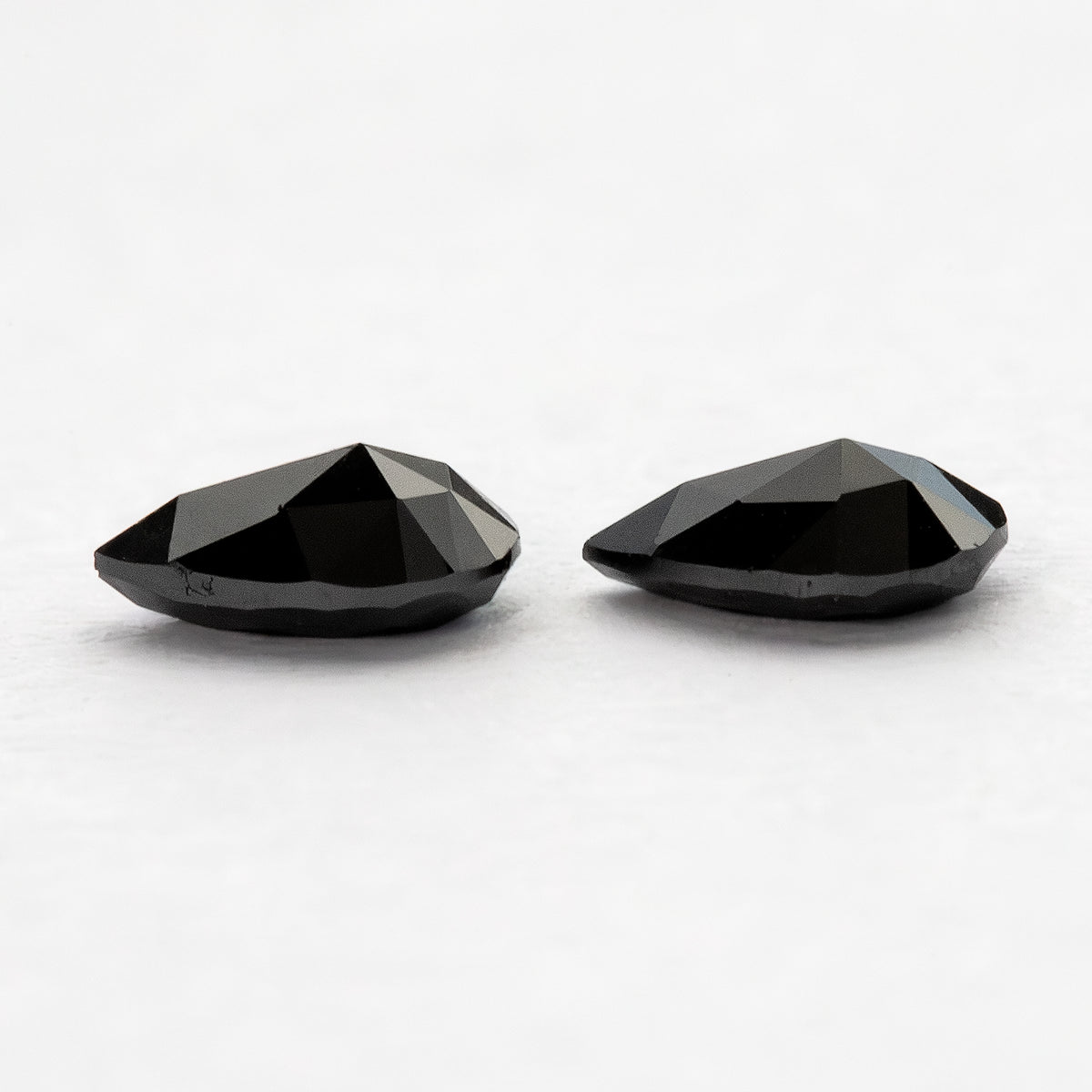 Low reverse-side profile of two black pear-shaped diamonds, showing the raised faceted undersides.