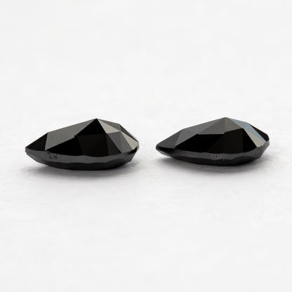 Low reverse-side profile of two black pear-shaped diamonds, showing the raised faceted undersides.