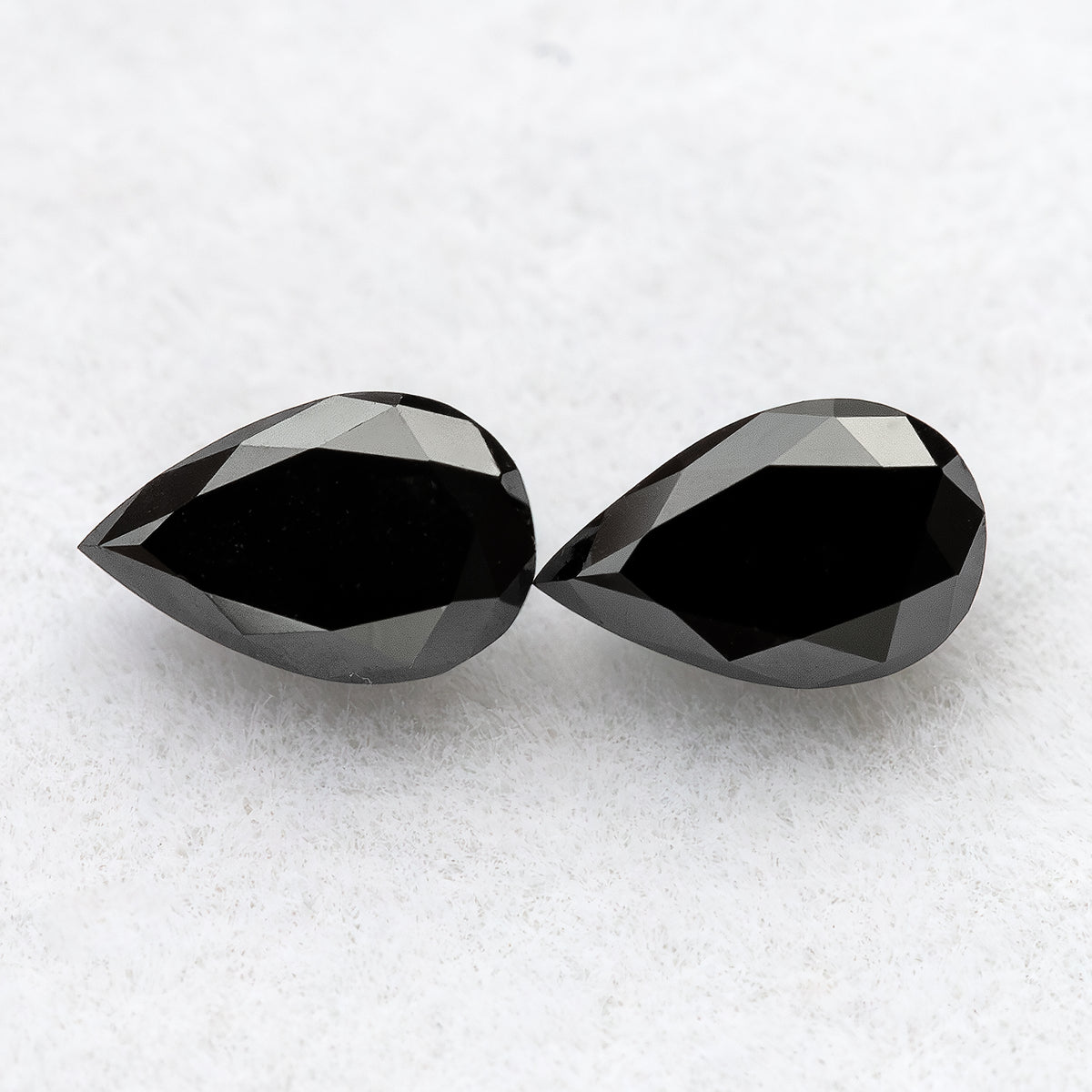 Close face-up view of two black pear-shaped diamonds on white, showing complete outlines, broad tables and crown facets.