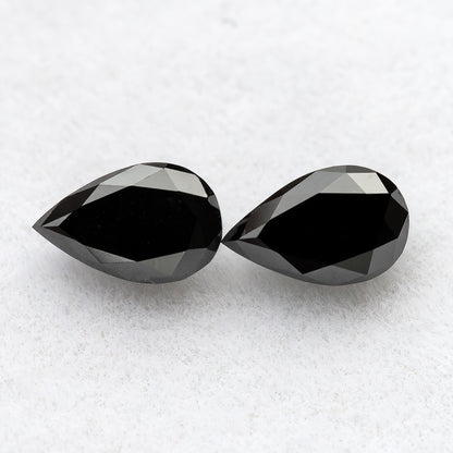 Close face-up view of two black pear-shaped diamonds on white, showing complete outlines, broad tables and crown facets.