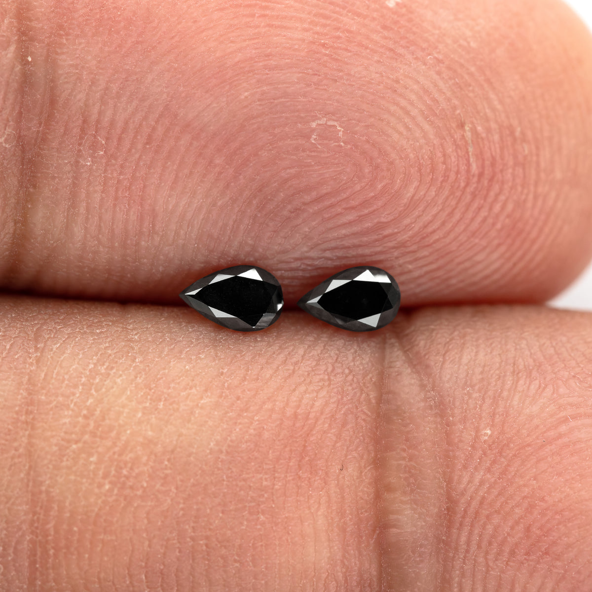 Black pear-shaped diamond pair resting on fingertips, with both faces and their small scale visible.