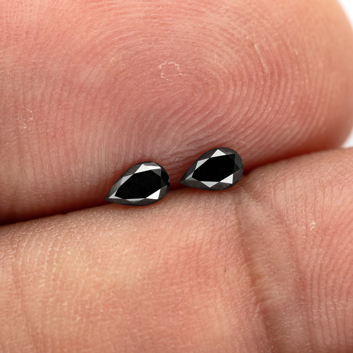 Two black pear-shaped diamonds placed diagonally on fingertips, showing their dark faces and reflective crown edges.