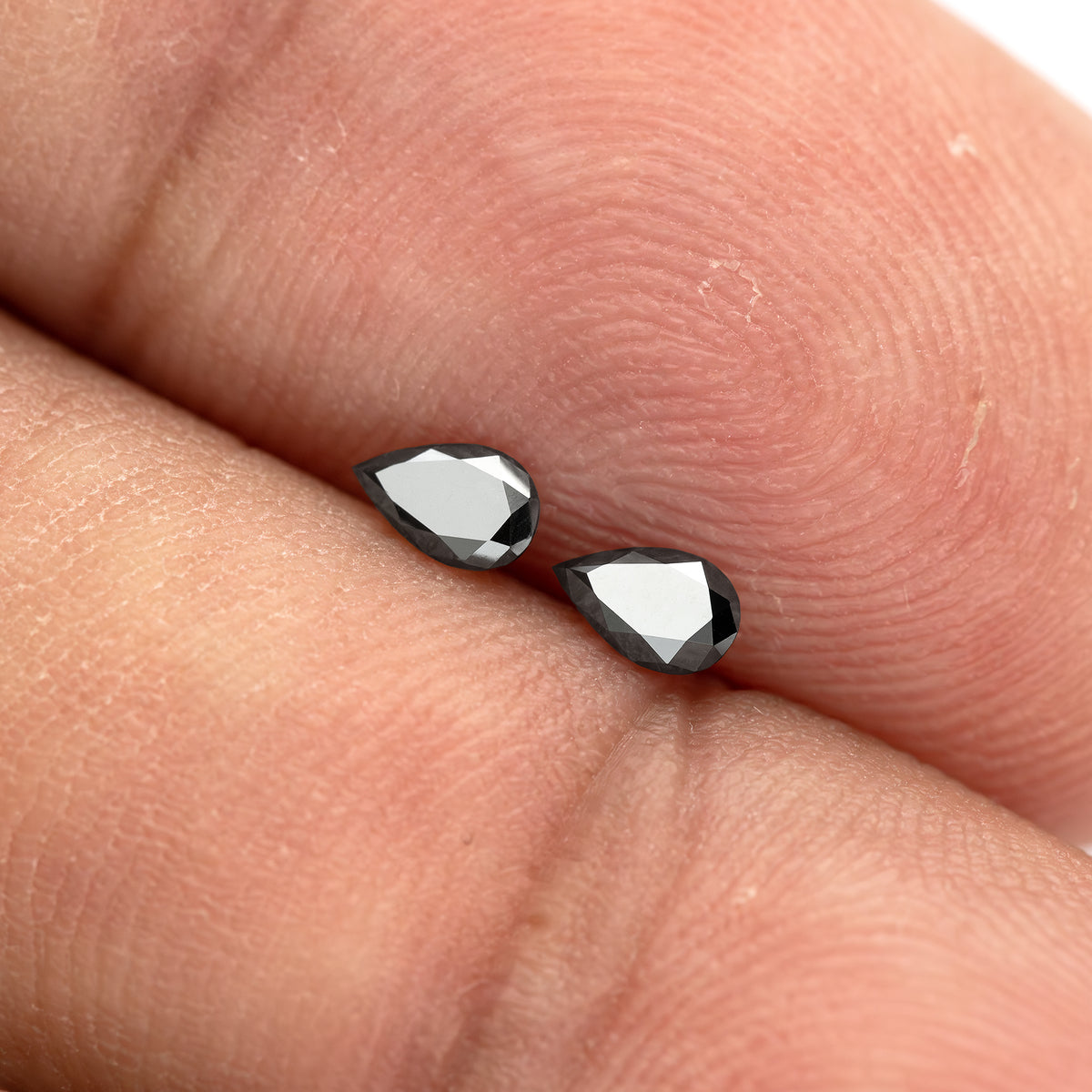 The black pear-shaped diamond pair on fingertips under a bright reflection, with both complete outlines visible.