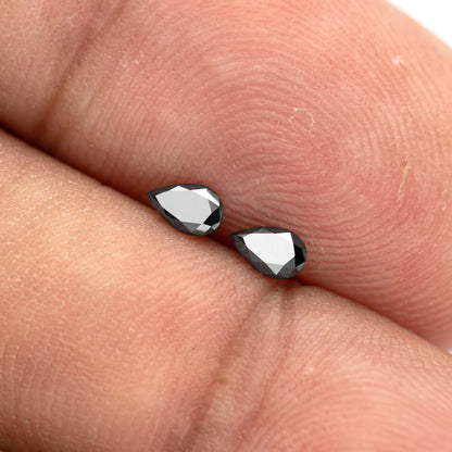 The black pear-shaped diamond pair on fingertips under a bright reflection, with both complete outlines visible.