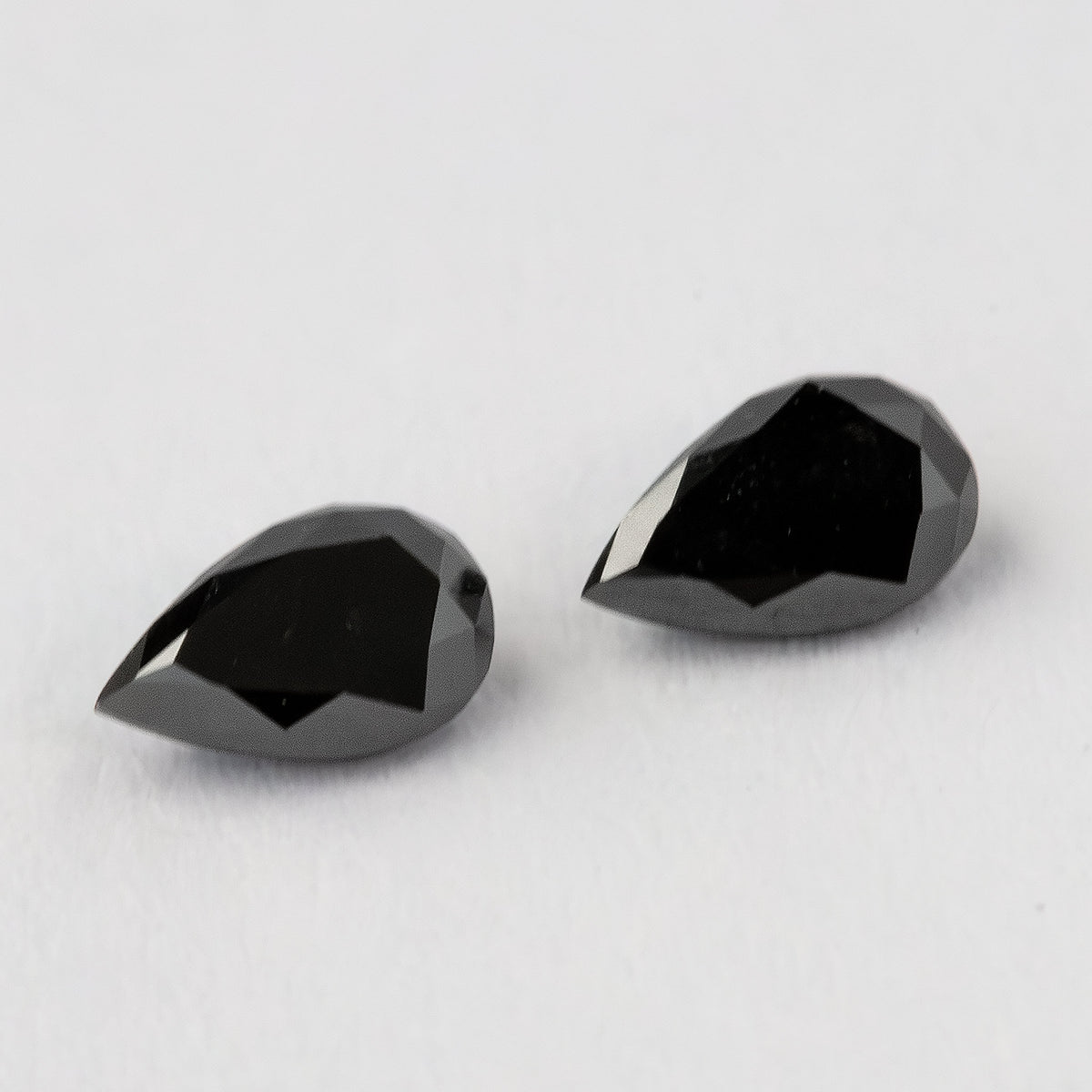 The two black pear-shaped diamonds face-up from an oblique angle, with dark tables and silver-gray edge reflections.