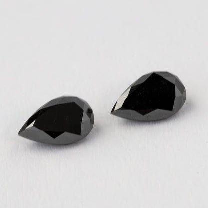 The two black pear-shaped diamonds face-up from an oblique angle, with dark tables and silver-gray edge reflections.