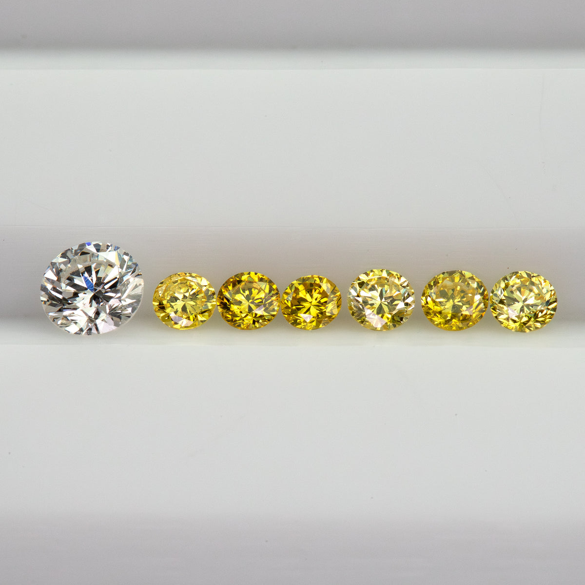 Horizontal row of six yellow diamonds on a white tray beside a white comparison diamond, not included.
