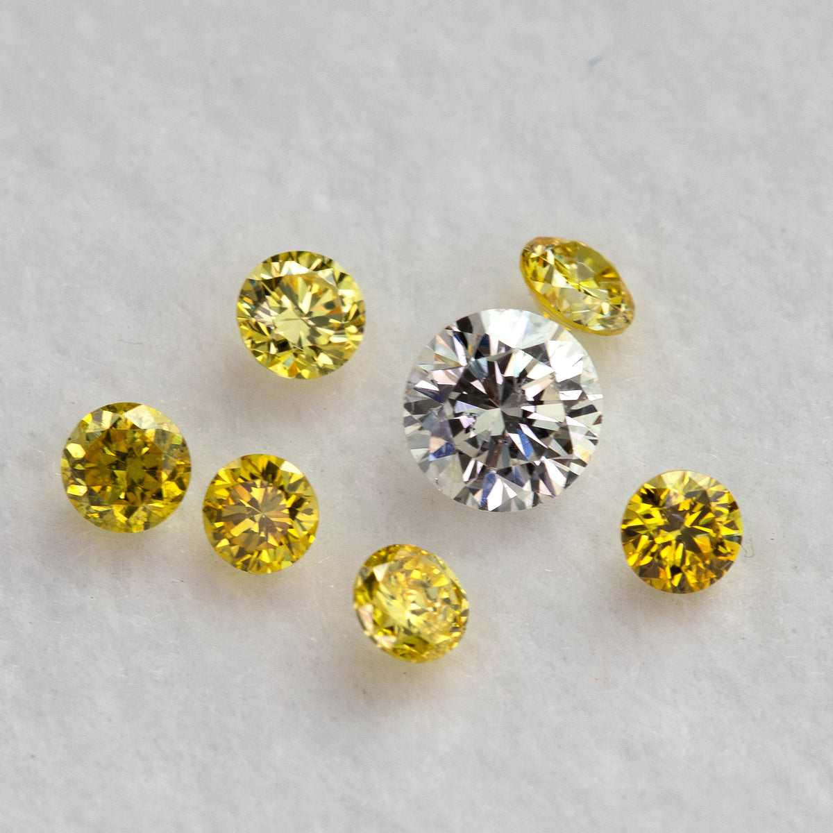 Six yellow diamonds loosely arranged around an excluded white comparison diamond on a pale surface.