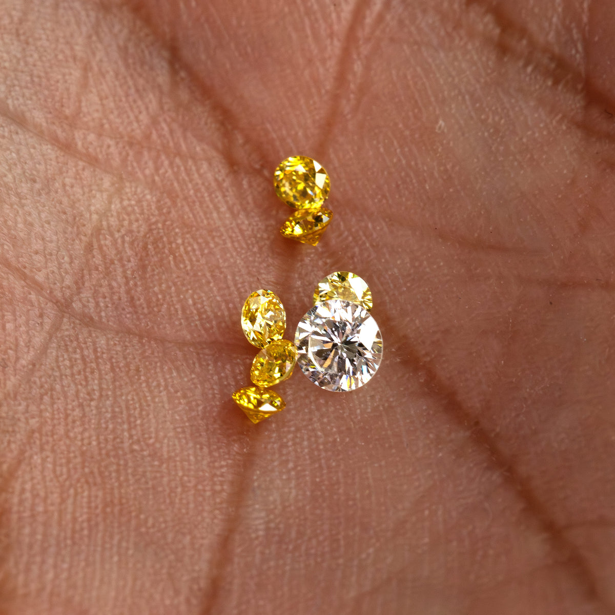 Yellow diamonds resting on a palm for scale beside a white comparison diamond, not included.