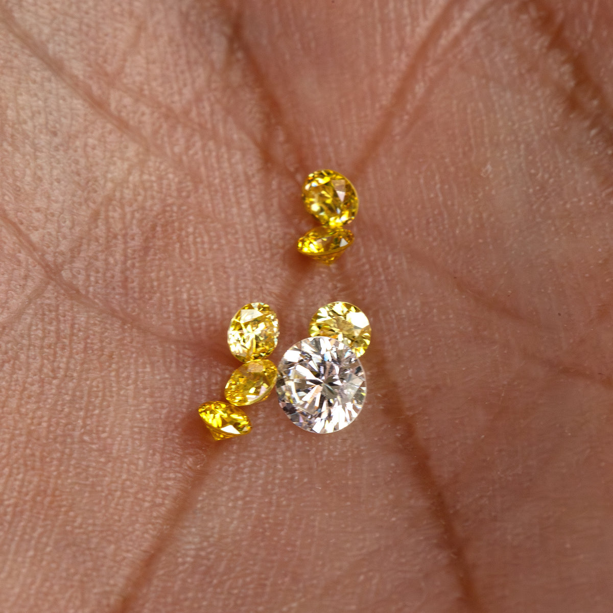 Alternate palm view of the yellow parcel with tilted stones; the white comparison diamond is excluded.