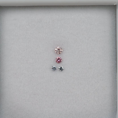 Wider face-up view of the four loose round diamonds centered on white padding, with two pink-looking stones over two smaller cool-toned stones.