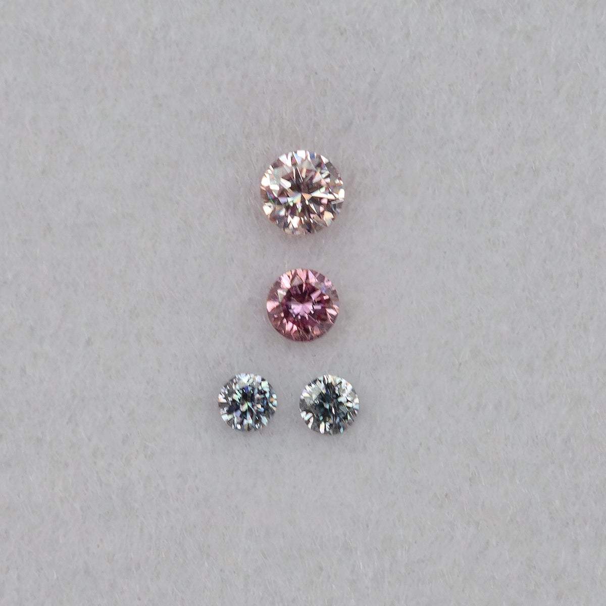 Four round diamonds viewed face-up in a straight arrangement, showing pale pink, purplish pink and cool-toned facet reflections.