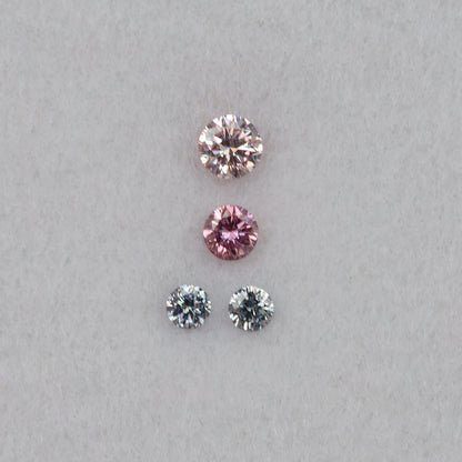 Four round diamonds viewed face-up in a straight arrangement, showing pale pink, purplish pink and cool-toned facet reflections.