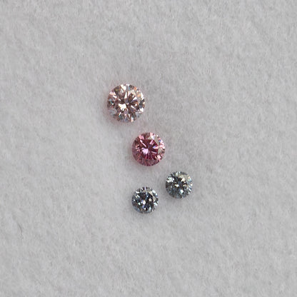 Face-up close-up of four loose round diamonds on white padding, two pink-looking stones above two smaller cool blue-gray stones.