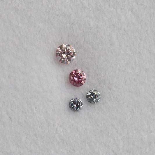 Face-up close-up of four loose round diamonds on white padding, two pink-looking stones above two smaller cool blue-gray stones.