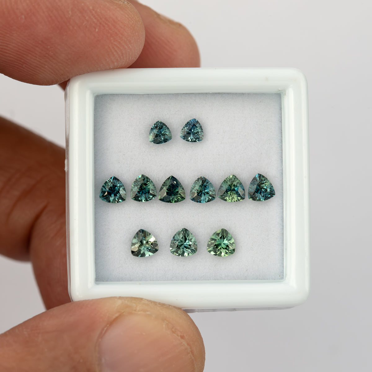 Closer hand-held view of the teal trillion sapphire lot, showing the three approximate size groups.