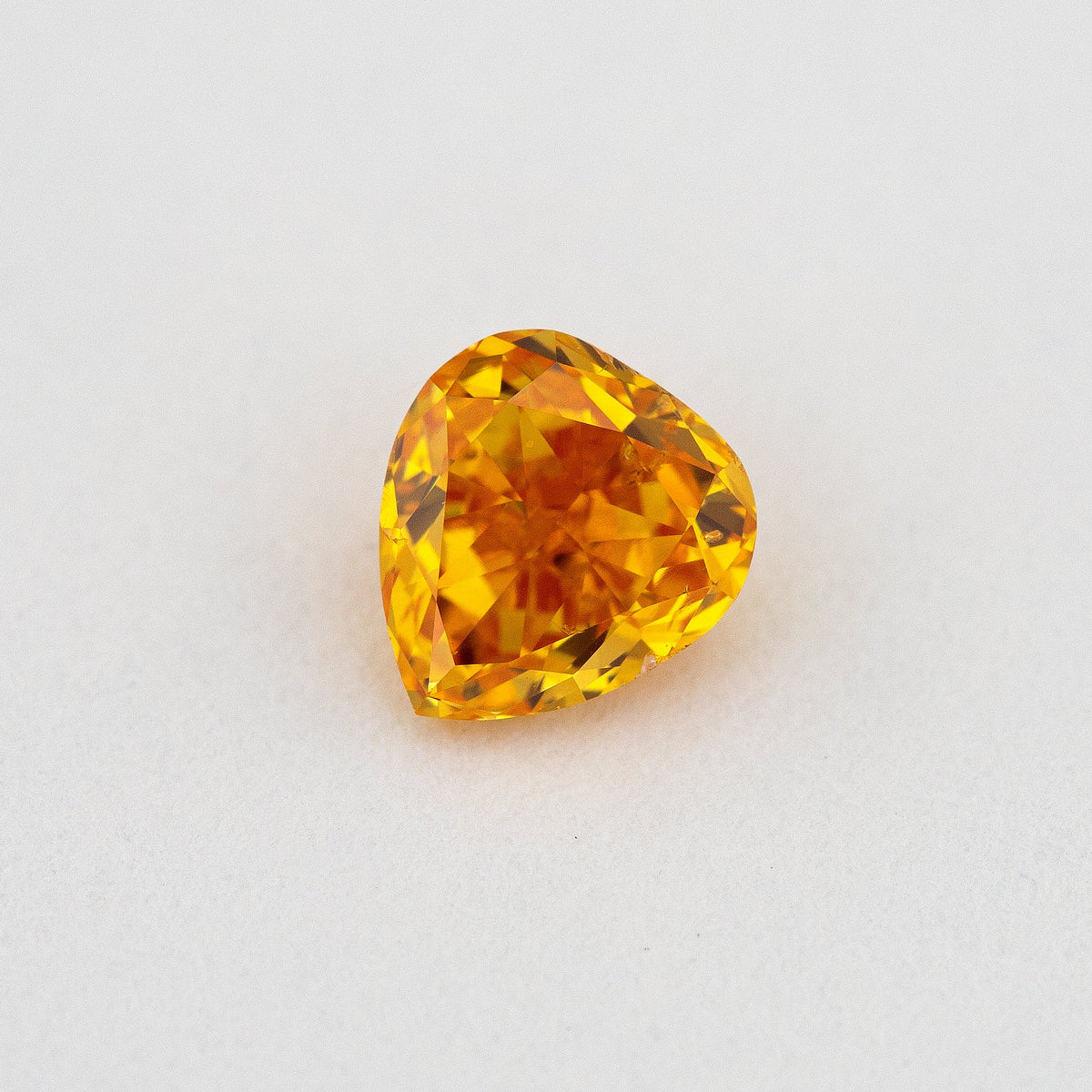 Face-up heart-shaped orange diamond on a pale surface, showing yellow flashes, its crown facets and pointed end.