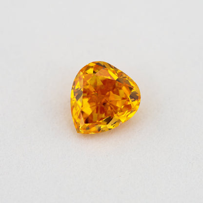 Face-up heart-shaped orange diamond on a pale surface, showing yellow flashes, its crown facets and pointed end.