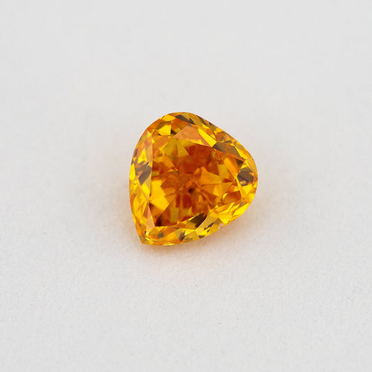 Face-up heart-shaped orange diamond on a pale surface, showing yellow flashes, its crown facets and pointed end.