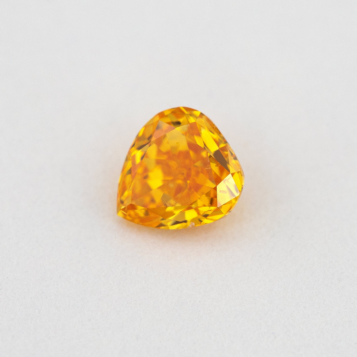 Angled crown view of the heart-shaped orange diamond, with bright yellow reflections across its upper facets.