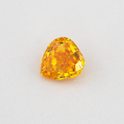 Angled crown view of the heart-shaped orange diamond, with bright yellow reflections across its upper facets.