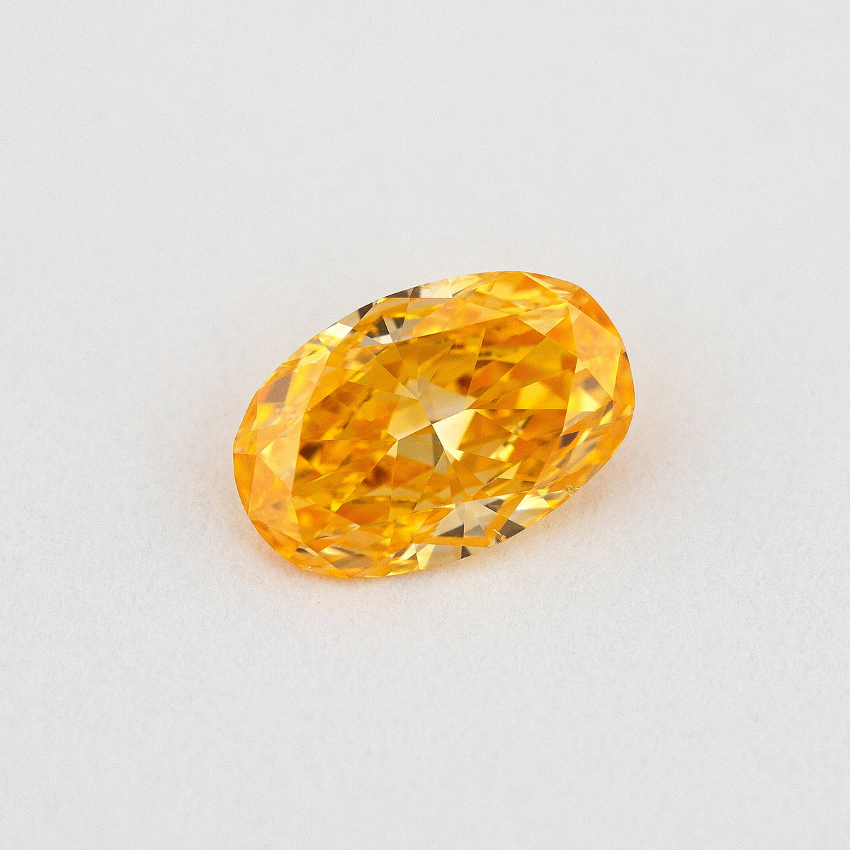 Face-up oval orange diamond on a pale surface, showing its elongated outline, central table and yellow flashes.