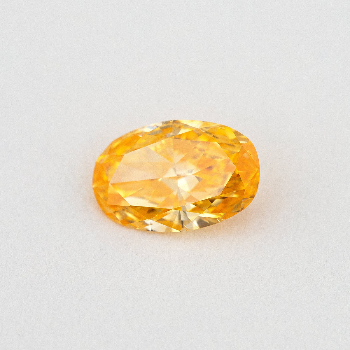 Angled crown view of the oval orange diamond, with broad bright facets and lighter yellow reflections.