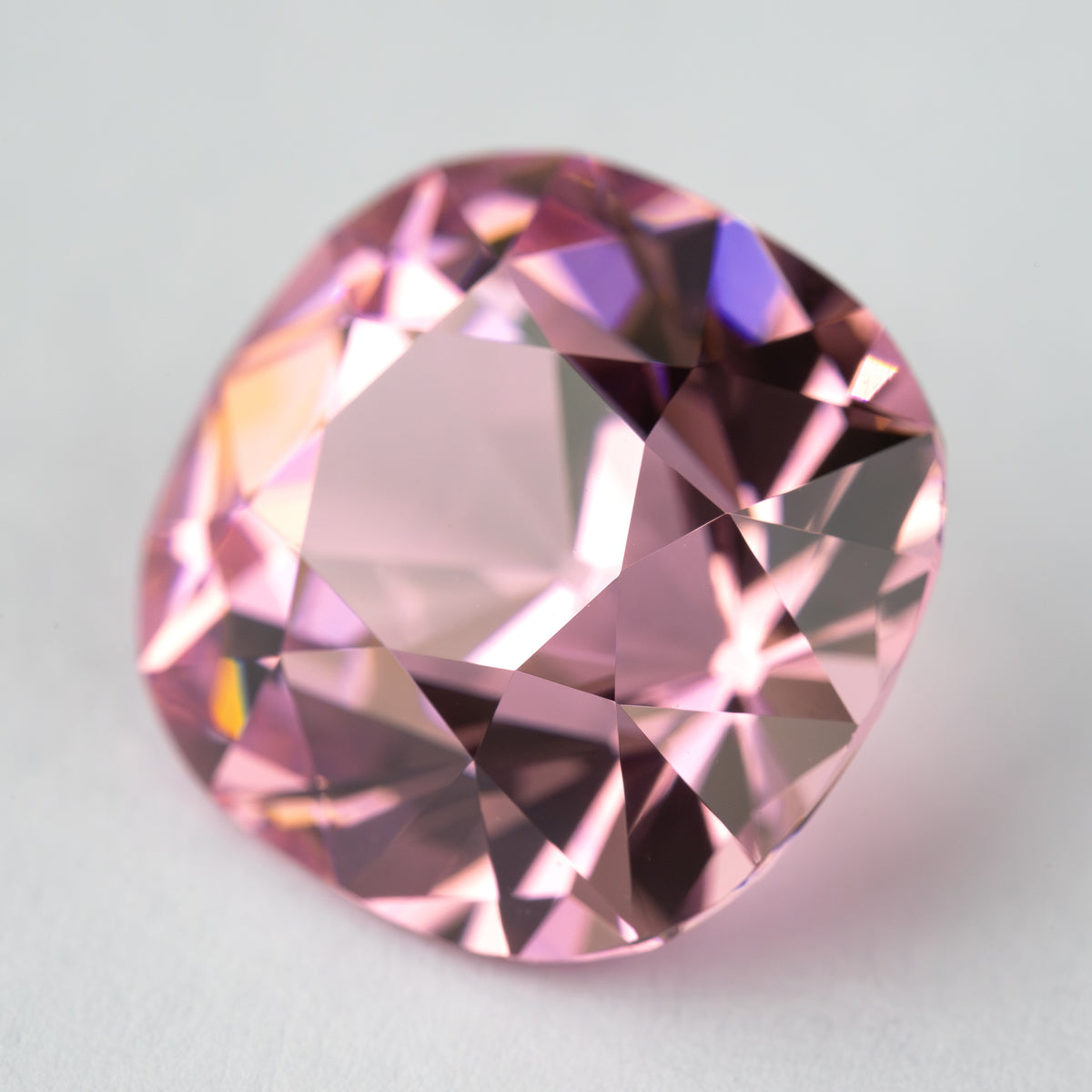 Pink cushion-shaped lab-grown YAG tilted face-up, showing changing light reflections. View 9.