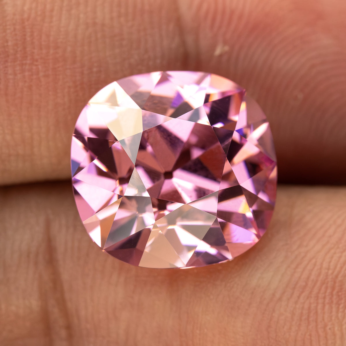 Pink cushion-shaped lab-grown YAG resting on fingertips for scale. View 3.