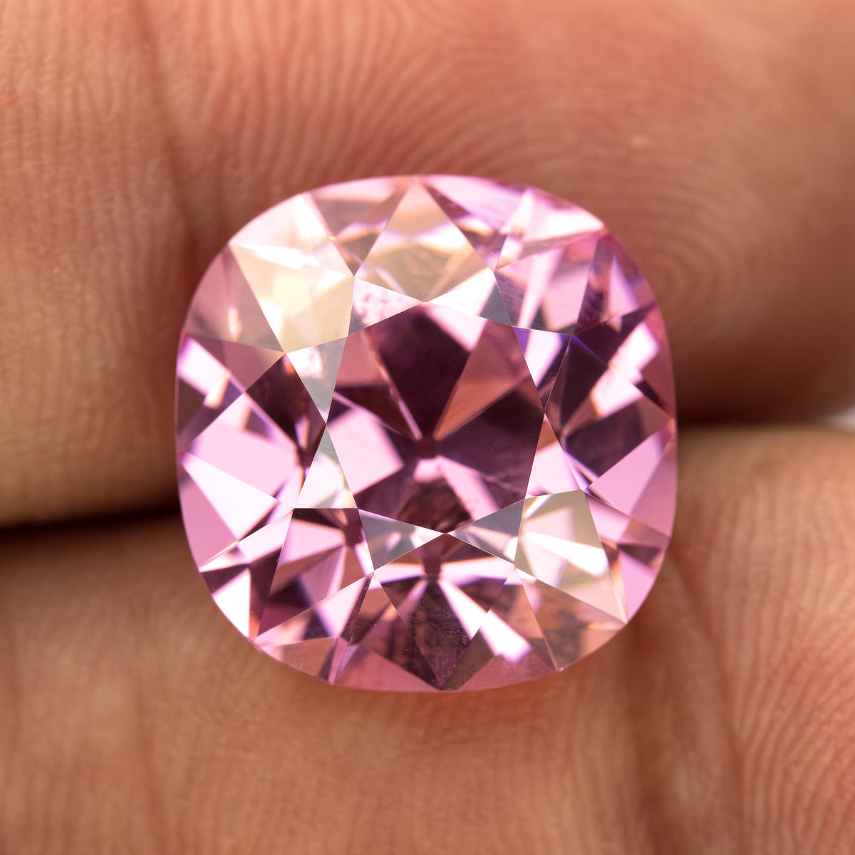 Pink cushion-shaped lab-grown YAG resting on fingertips for scale. View 4.