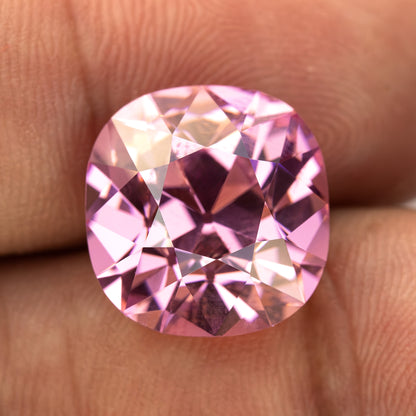 Pink cushion-shaped lab-grown YAG resting on fingertips for scale. View 4.