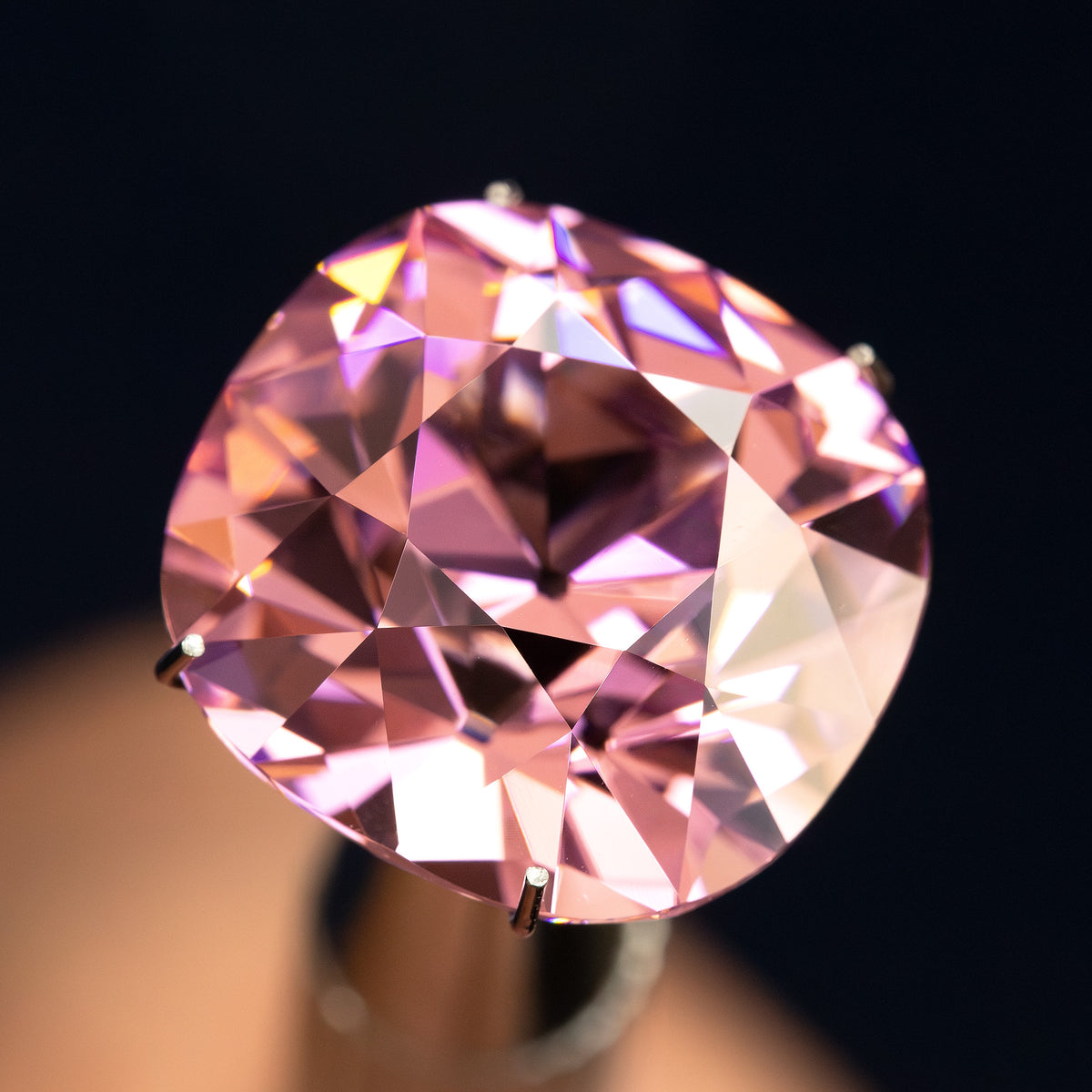 Pink cushion-shaped lab-grown YAG tilted face-up, showing changing light reflections. View 6.