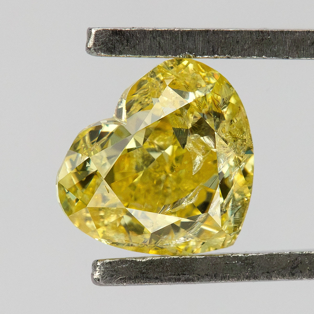 Yellow heart-shaped diamond held at an angle in tweezers, showing the cleft, pointed tip and visible internal markings.