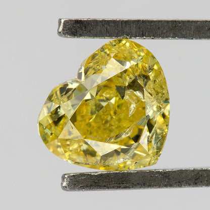 Yellow heart-shaped diamond held at an angle in tweezers, showing the cleft, pointed tip and visible internal markings.