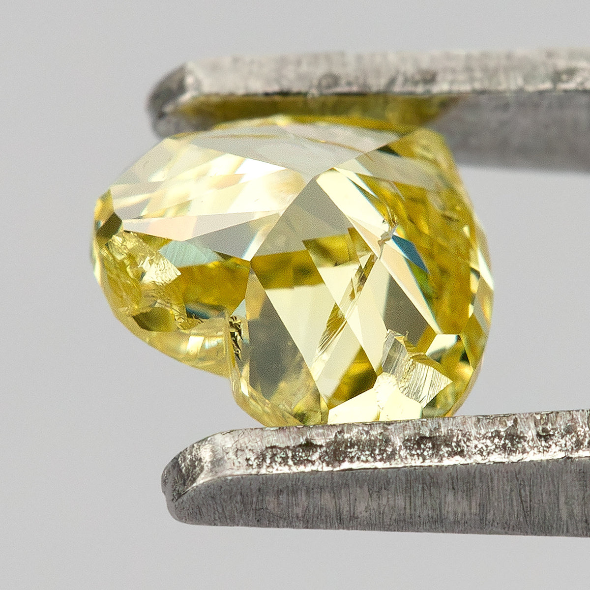 Oblique back view of the yellow heart-shaped diamond in tweezers, showing pavilion facets and bright reflections.