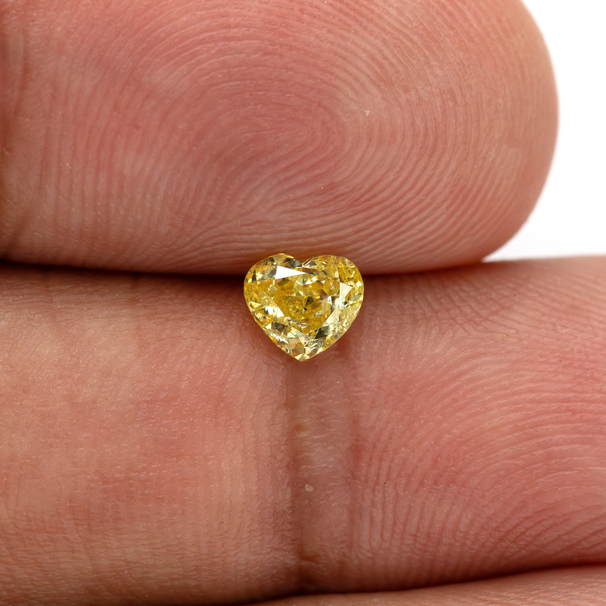 Yellow heart-shaped diamond resting upright between fingertips, with the cleft at the top and the point below.
