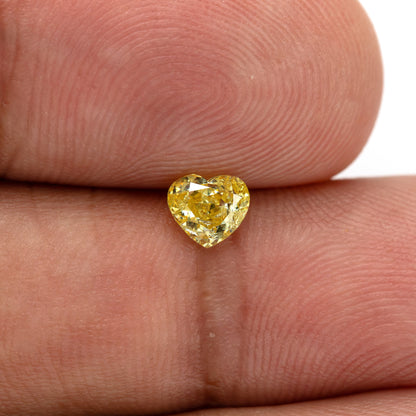 Yellow heart-shaped diamond resting upright between fingertips, with the cleft at the top and the point below.