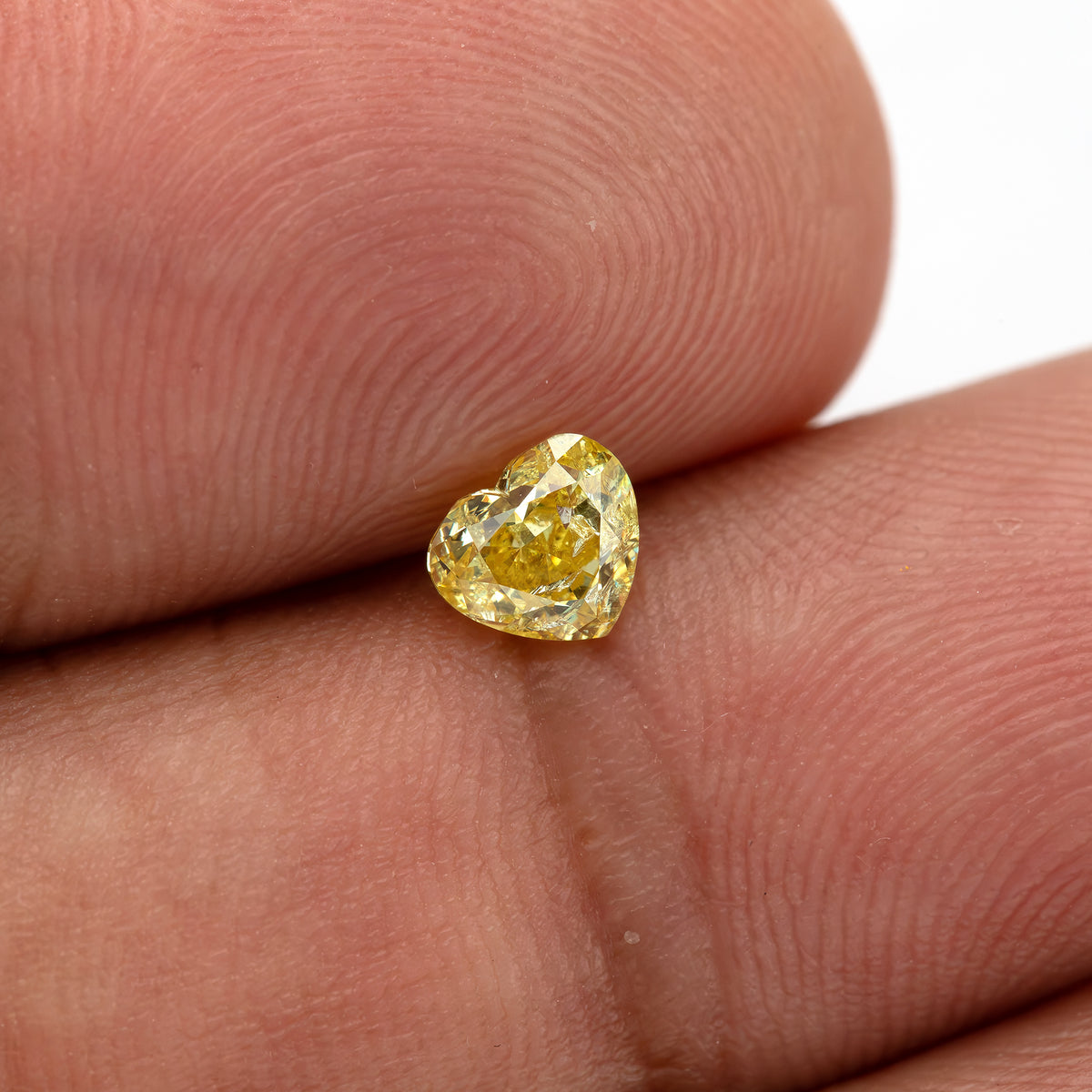 Yellow heart-shaped diamond tilted on a fingertip, showing its small size and brighter upper facets.