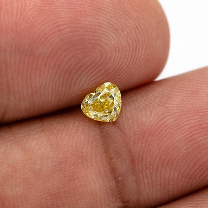 Yellow heart-shaped diamond tilted on a fingertip, showing its small size and brighter upper facets.