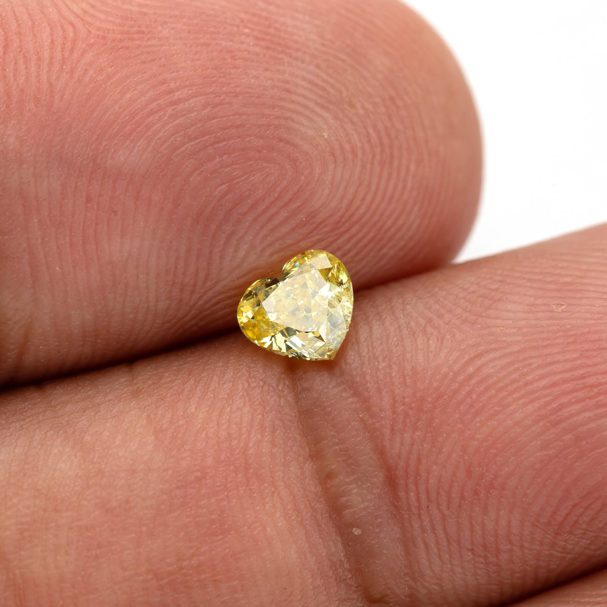 Yellow heart-shaped diamond on fingertips with a broad pale reflection obscuring part of its center.