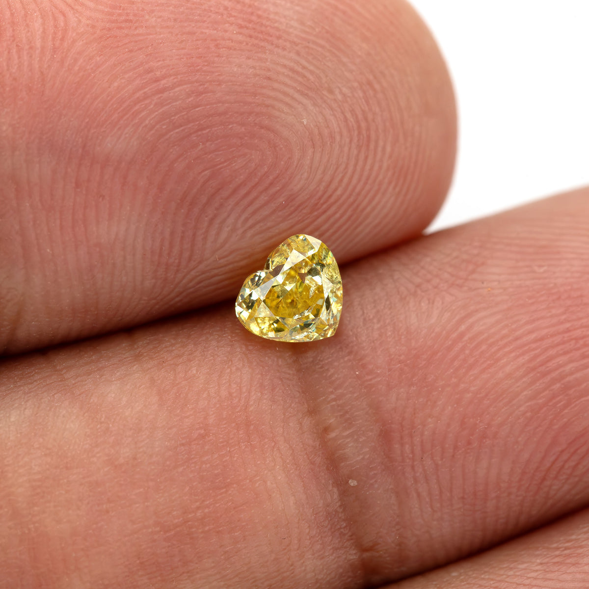 Small yellow heart-shaped diamond resting against fingertips, with a narrow bright reflection near its lower edge.
