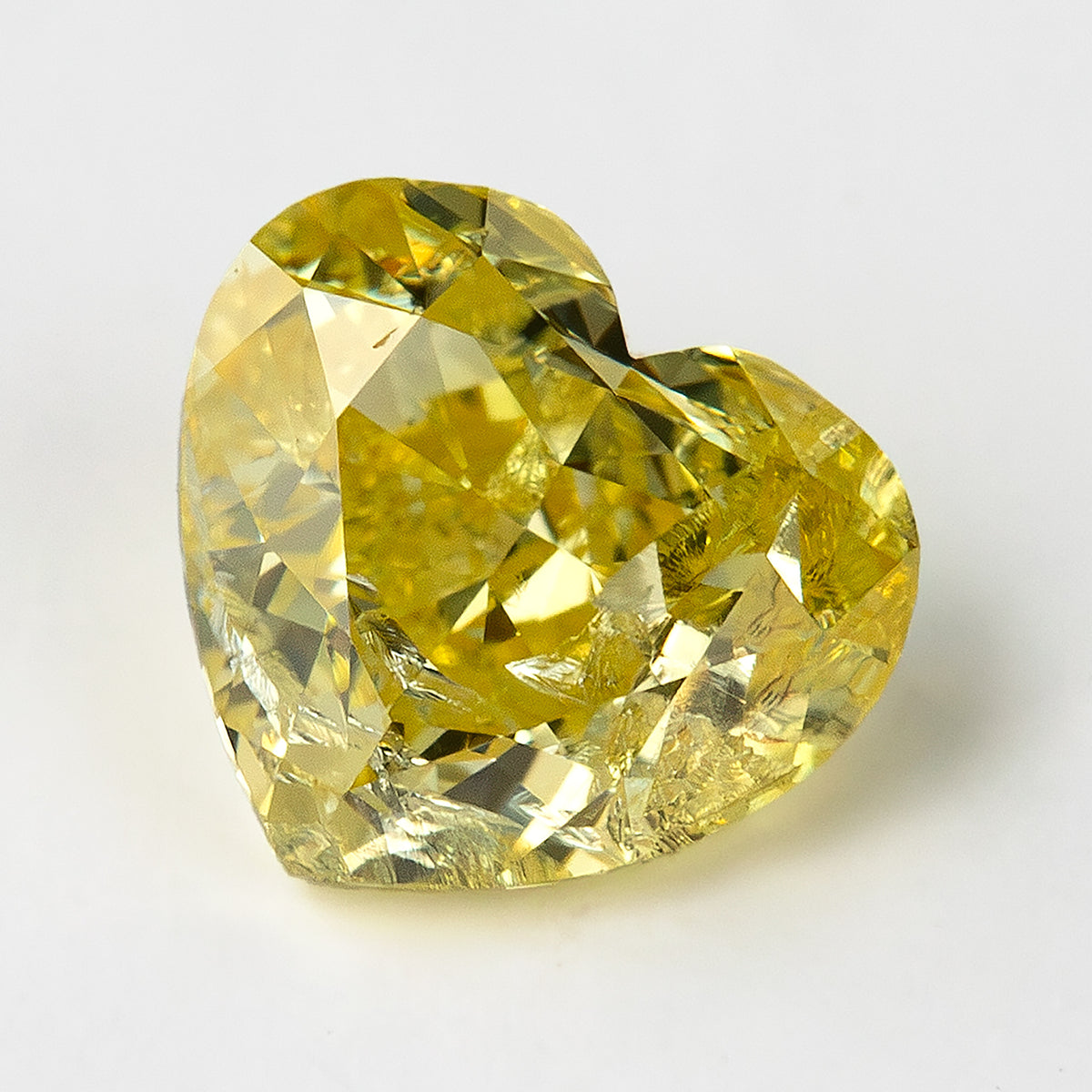 Yellow heart-shaped diamond on a pale surface, leaning slightly to one side with internal markings visible through the crown.